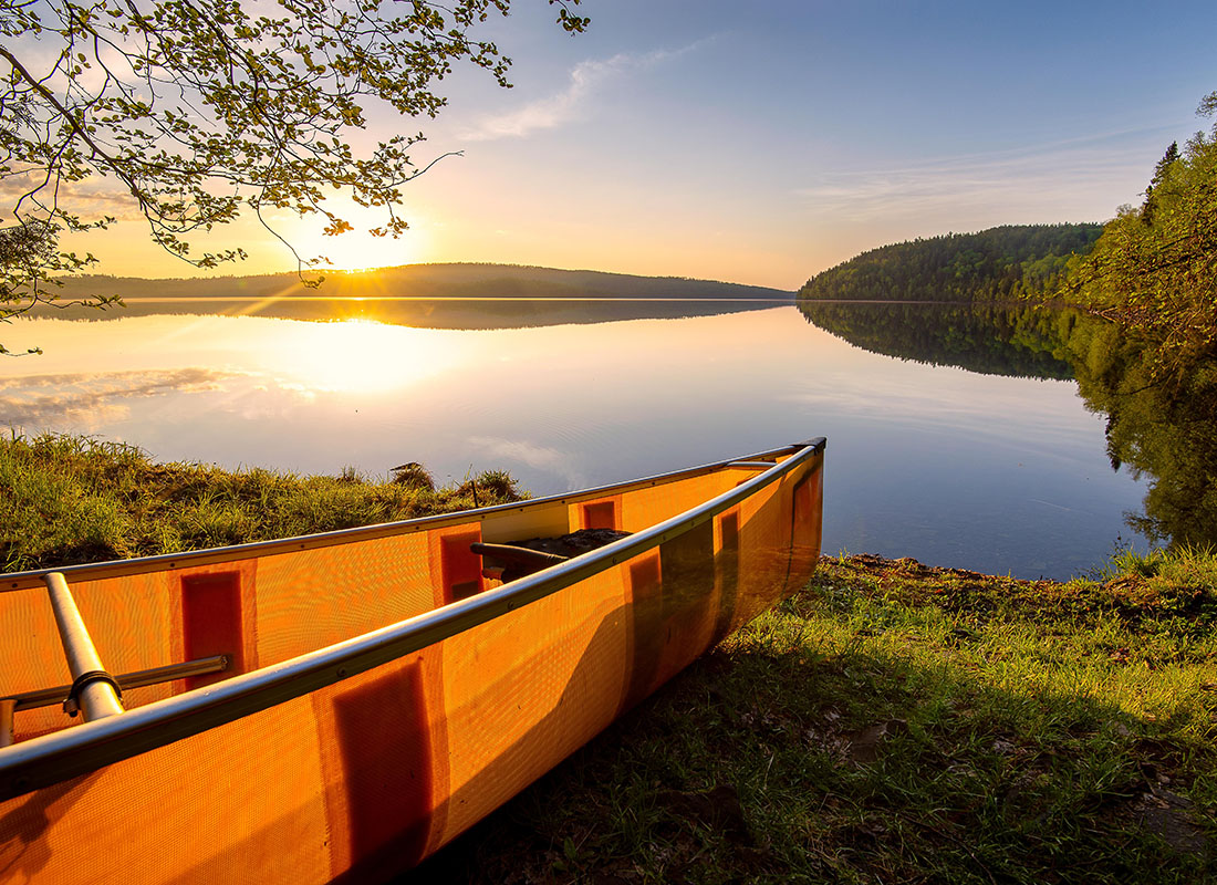 We Are Independent - Scenic View of an Orange Canoe Laying on the Grass Next to a Lake at Sunset